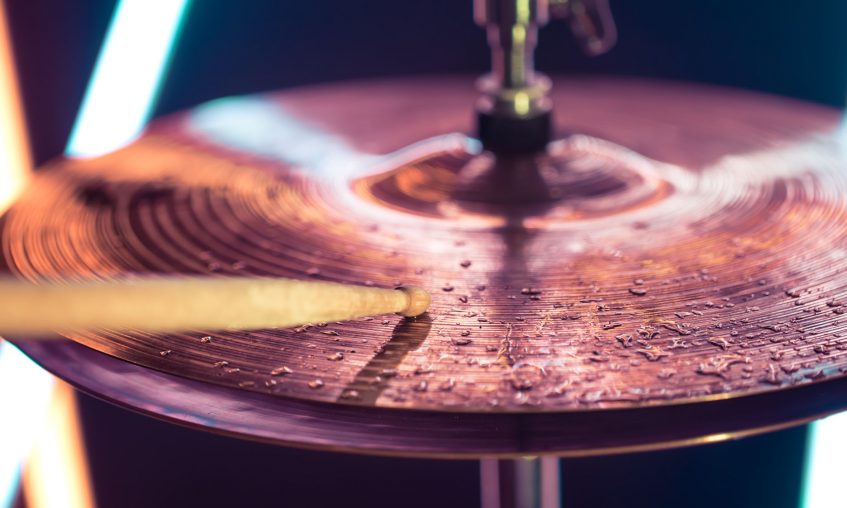 Hi-hat close-up of plates with drumsticks Hi-hat close-up of plates with drumsticks on a background of colored lanterns. Water drops on plates. Musical concept with a working drum.