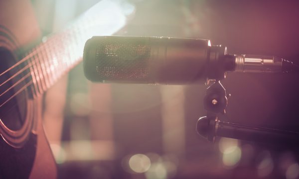 The Studio microphone records an acoustic guitar close-up. Beautiful blurred background of colored lanterns. The Studio microphone records an acoustic guitar close-up, in a recording Studio or concert hall, with a drum set on a background in out-of-focus mode. Beautiful blurred background of colored lanterns