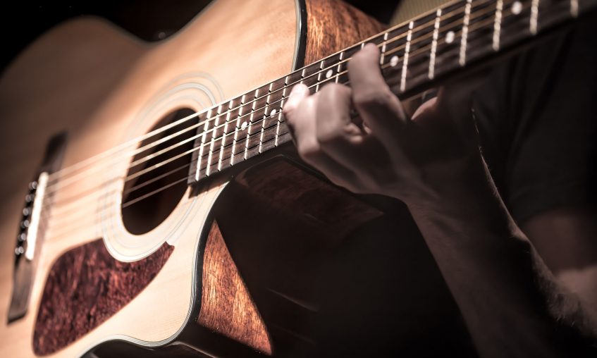 Man playing acoustic guitar on dark background. A musical concept. Man playing acoustic guitar on dark background, guitar closeup. A musical concept.